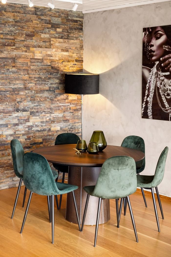 about-img Chic café interior featuring a round table with green velvet chairs, a stone accent wall, and stylish decor.