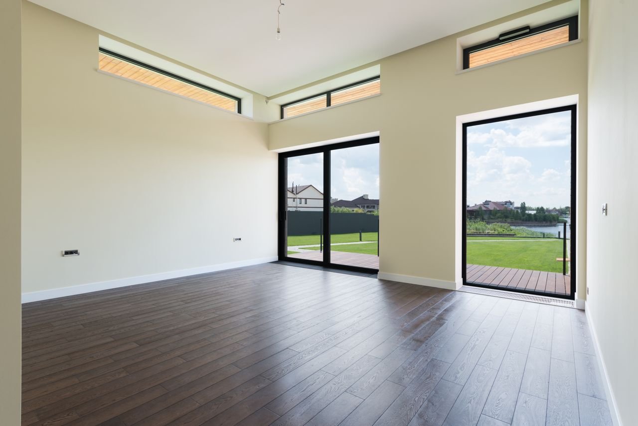 hero-img-01 Interior of spacious room with wooden laminate floor big windows and glass door viewing terrace and green lawn