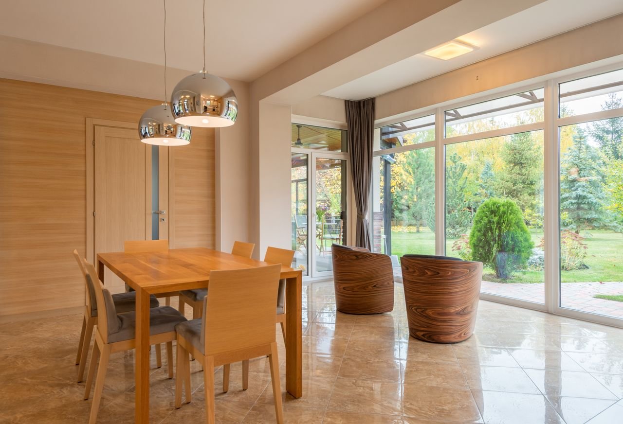 about-01 Interior of spacious dining zone with panoramic windows furnished with wooden table and chairs on tilled floor in villa